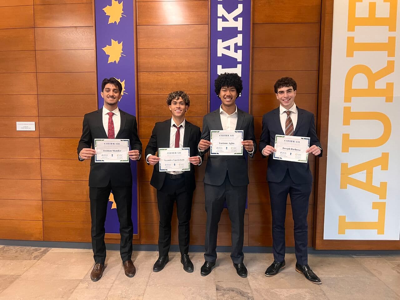 Jasman Mander and his three teammates holding LSCA × LEC certificates in front of a Laurier banner.
